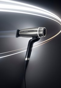 Sèche-cheveux ghd Speed noir et argent élégant avec des lignes de flux d'air sur un fond dégradé sombre, montrant l'interrupteur d'alimentation et le cordon.