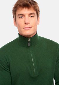 Pull vert zippé avec col montant, texture côtelée et demi-fermeture éclair à l'avant. Présente un tissu lisse et des détails subtils sur la fermeture.