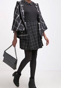 Black and gray checkered skirt with a fitted black top and a plaid open jacket. Black ankle boots and a black handbag with a chain strap.