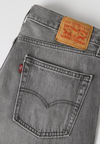 Πίσω τσέπη σε γκρι τζιν Levi's με χαρακτηριστική κόκκινη ετικέτα και καφέ δερμάτινη ετικέτα μάρκας που δείχνει δύο άλογα.