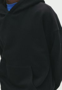Sort hætte sweatshirt lavet af blødt materiale med en frontlomme og diskret logo-detaljering. Har en afslappet pasform og ribbede manchetter.