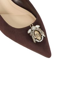 Brown suede pointed-toe pump featuring a decorative gold and crystal brooch accent at the front. Smooth interior lining.