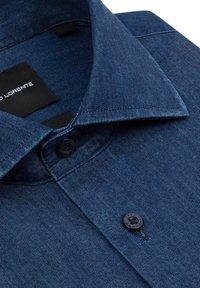 Koszula dżinsowa w ciemnoniebieskim kolorze z subtelną fakturą, z zaostrzonym kołnierzykiem i dwoma czarnymi guzikami z przodu. Metka widoczna wewnątrz kołnierzyka.