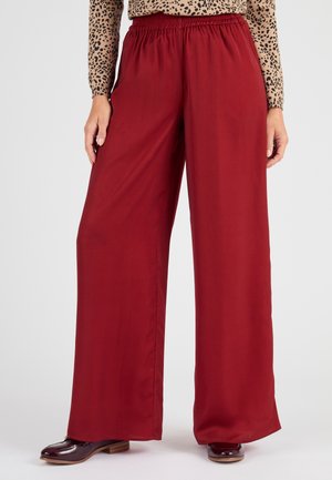 Wijd gevallen rode broek met een elastische tailleband, gemaakt van gladde stof. Gecombineerd met glanzende bruine instappers.
