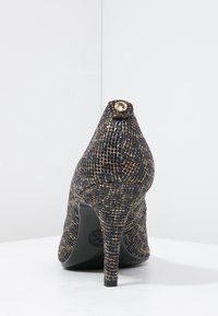 Chaussure à talon haut en matériau texturé noir et doré avec un bout pointu et un bouton doré décoratif à l'arrière, dotée d'un talon aiguille fin.