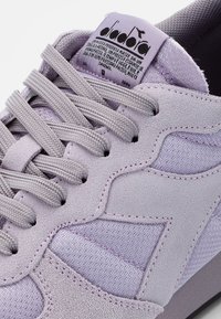 Fioletowy zamszowy trampek z fakturowanymi tkaninowymi wstawkami. Posiada płaskie sznurowadła, wyściełany język oraz metkę z logo na kołnierzu.