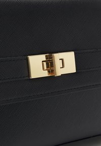 Sac à main noir texturé avec un fermoir doré lisse et des détails en accent. Doté d'une forme structurée et de coutures discrètes pour un design épuré.