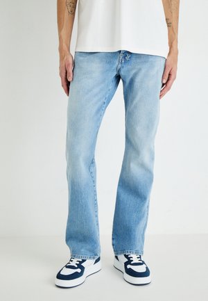Light blue denim jeans with a straight cut, subtle fading, and five-pocket design, paired with navy and white sneakers.