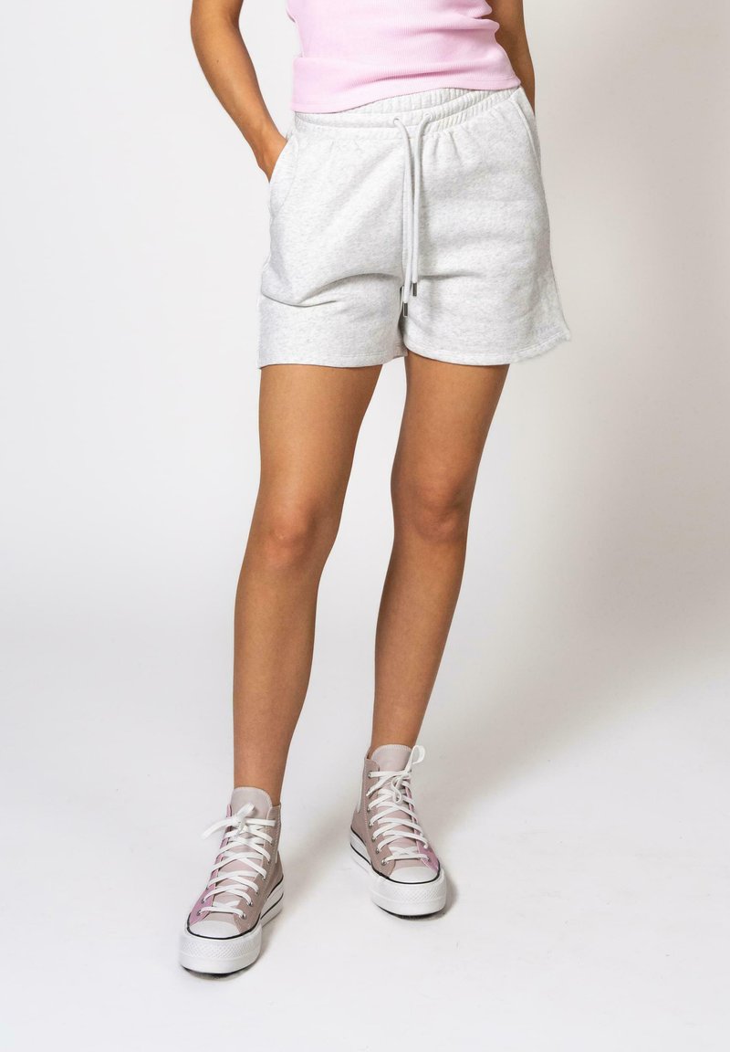 Shorts en coton gris avec une taille élastique et un cordon de serrage, associés à des baskets montantes beiges et blanches, avec des lacets roses.
