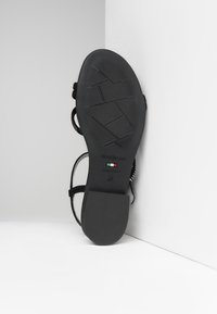 Sandalo nero con suola in gomma testurizzata, cinturini regolabili e design minimalista. Presenta il logo, la bandiera italiana e la taglia 37.