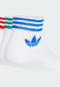 Bele nogavice do gležnjev v beli barvi s stripe v modri, zeleni in rdeči barvi na robovih, z modrim logotipom Adidas na strani. Mehka, pletena tekstura.