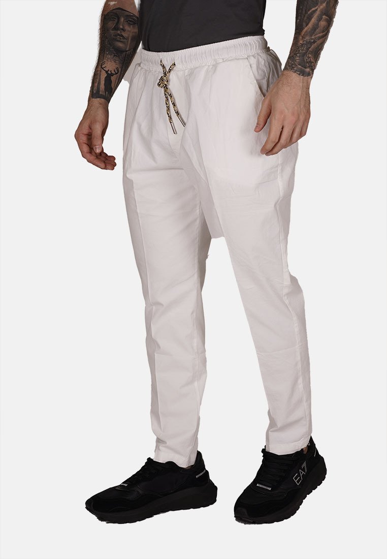 Pantalones jogger blancos, ligeros, con cintura elástica y cordón. Presenta bolsillos y un ajuste holgado. Combinados con zapatillas negras.