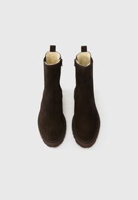 Καφέ μποτάκια από σουέτ με υφή, εσωτερική επένδυση από γούνα και φερμουάρ στο πίσω μέρος. Επίπεδη λαστιχένια σόλα με ραφές γύρω από την άκρη.