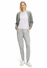Grijze gebreide cardigan over een wit T-shirt, gecombineerd met grijze sweatpants en witte sneakers. De outfit heeft een ontspannen pasvorm.