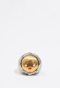 Broche redonda de oro y plata con un diseño de cara de sol, adornada con gemas transparentes alrededor del borde y con características faciales pintadas.