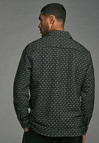 Black patterned shirt featuring a diamond design, button-down collar, long sleeves, and textured fabric, viewed from the back.