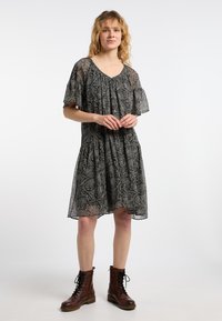 Musta kuviollinen mekko, jossa on lyhyet lentosuorat hihat, röyhelökaulus ja kerätty hameosa. Yhdistetty ruskeisiin nauhakenkiin nilkkamittaisina.