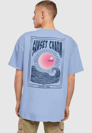 Light blue cotton t-shirt featuring a graphic print on the back: a pink sunset, waves, and text "SUNSET CHARM" with a retro design.