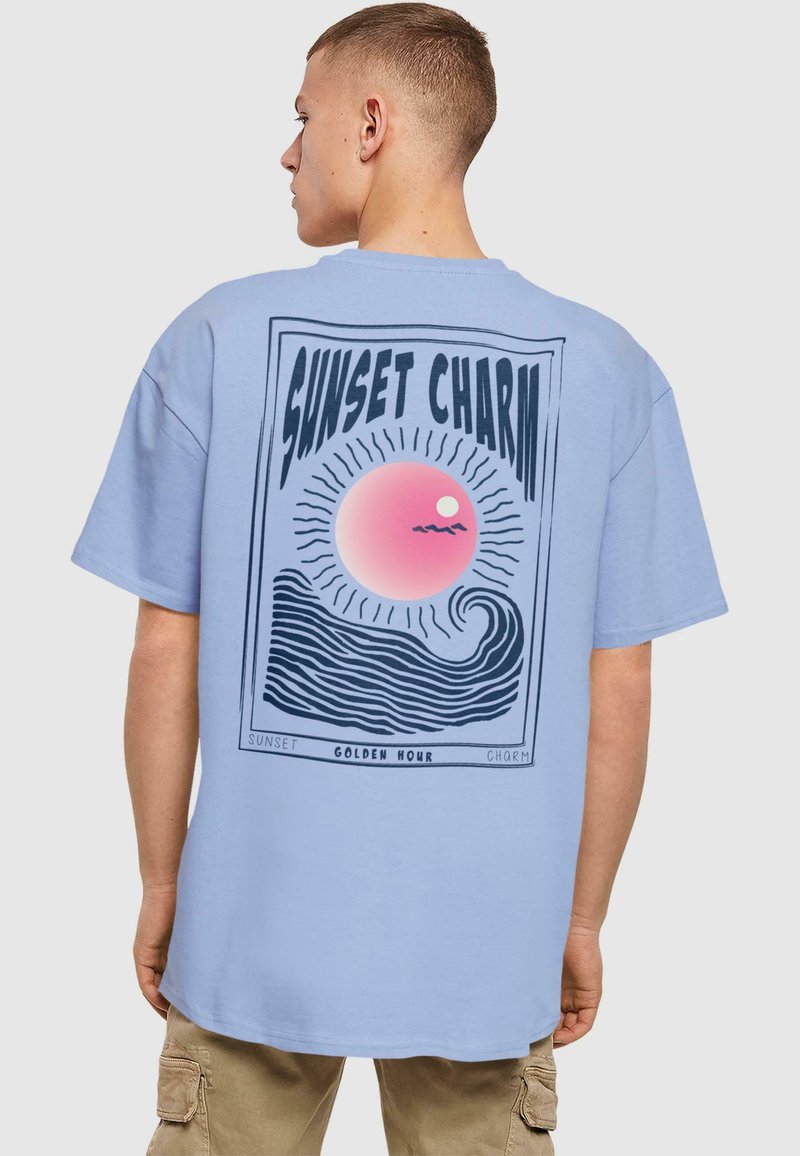 Világoskék pamut póló, hátul grafikával: rózsaszín naplemente, hullámok és a "SUNSET CHARM" felirat retro dizájnnal.