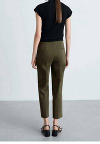 Czarny krótki top z rękawem, zestawiony z oliwkowymi spodniami o dopasowanym kroju. Spodnie mają gładką fakturę i dwie tylne kieszenie. Czarne sandały na obcasie.