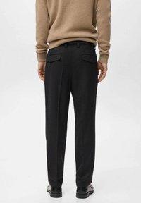 Pantalones negros con un corte ajustado, que presentan dos bolsillos traseros y una textura suave. Combinados con un suéter de punto beige.