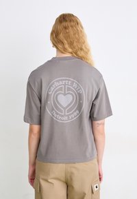 T-shirt grigia in cotone con maniche corte, con una grande grafica circolare sul retro che recita "Carhartt WIP Detroit 1989."