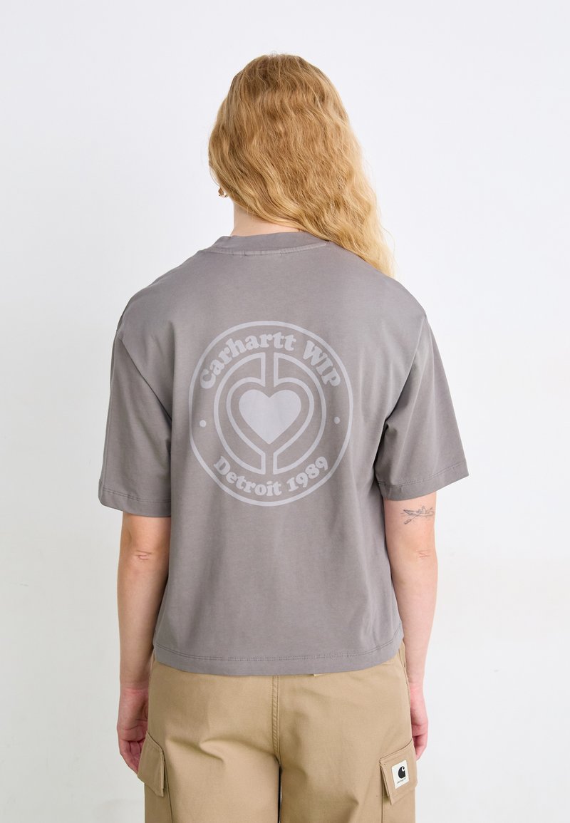 T-shirt grigia in cotone con maniche corte, con una grande grafica circolare sul retro che recita "Carhartt WIP Detroit 1989."