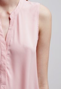 Blusa senza maniche rosa realizzata in tessuto morbido, caratterizzata da un sottile scollo a V e dettagli di cucitura visibili, che presenta un design pulito e minimalista.