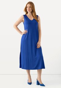Abito blu senza maniche con scollatura a V e spacco laterale; realizzato in tessuto morbido; indossato con scarpe con tacco alto blu coordinato.