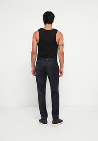 Top preto sem mangas combinado com calças escuras azul-marinho. As calças apresentam detalhes de bolsos laterais e traseiros. O calçado é preto com solas claras.