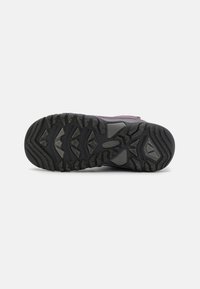 Semelle en caoutchouc noir avec des rainures profondes, présentant une combinaison de surfaces texturées et lisses, et un matériau extérieur violet avec des accents subtils.