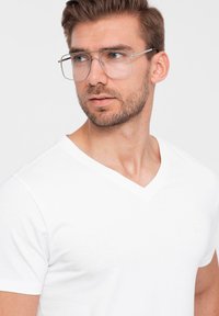 Weißes Baumwoll-V-Ausschnitt-T-Shirt mit kurzen Ärmeln, mit einem kleinen Logo auf der linken Brust, glatter Textur und klassischem Schnitt. Klare Brille.