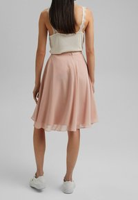 Ljusrosa kjol i A-linjeform av flytande tyg med slät yta och elastisk midja, kombinerad med en beige topp med spetskant.