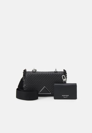 Musta kudottu olkalaukku leveällä hihnalla ja kolmiomaisella metallikoristeella, mukana pieni musta korttikotelo hopeisella logotekstillä.