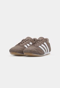 Suede athletic shoes in brown with white stripes. Features a low profile design, textured upper, and rubber sole for traction.