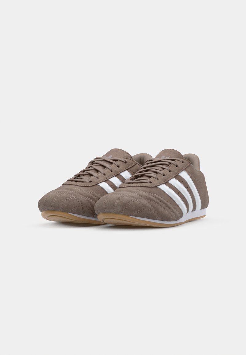 Braune Wildledersportschuhe mit weißen Streifen. Verfügt über ein niedriges Profil, eine strukturierte Oberseite und eine Gummisohle für besseren Halt.