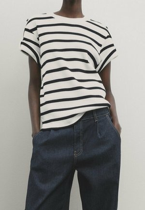 Wit geribd T-shirt met horizontale marineblauwe strepen, korte dolmanmouwen, gecombineerd met wijde donkerblauwe jeans met voorzakken.