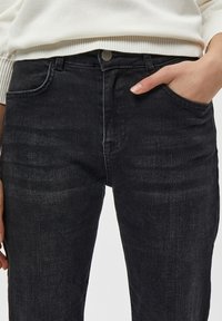 Vaqueros de mezclilla negra con corte slim, con una textura desgastada, diseño de cinco bolsillos y cierre de botón metálico en la cintura.