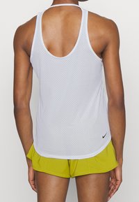 Vit nätad träningslinne med racerback-design, med rundad nederkant och svart Nike-logotyp på vänstra nedre sidan.