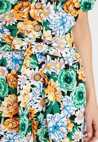 Odzież w kwiatowy wzór z żywymi żółtymi, pomarańczowymi, niebieskimi i zielonymi kwiatami na czarnym tle. Zawiera drewniane guziki i związany pasek.