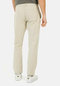Beige bomuldsbukser med lige snit, elastisk talje og en enkelt baglomme. Båret med hvide sneakers, der viser et rent, minimalistisk design.