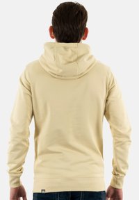 Sudadera con capucha color beige, con cordón ajustable, puños acanalados y cinturilla. Textura suave, costuras mínimas y un pequeño logo en el dobladillo.
