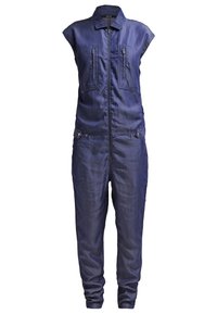 Combinaison sans manches en denim bleu foncé avec fermeture éclair à l'avant, deux poches poitrine zippées et pattes boutonnées aux hanches.