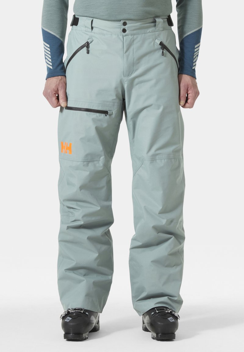 Lichtgroene waterdichte skibroek met ritszakken en een verstelbare taille; oranje logo op de linker dij; gladde, duurzame stof.