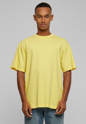 Yellow cotton t-shirt with a relaxed fit, short sleeves, and a crew neckline. Smooth texture without patterns. Worn over light blue jeans.