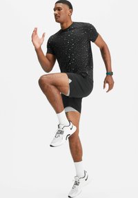 Schwarzes sportliches T-Shirt mit bunten Sprenkeln, kombiniert mit schwarzen Shorts mit grauen Akzenten, weißen Sneakers und weißen Kniestrümpfen.