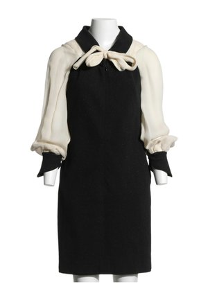 Robe noire sans manches avec de longues manches bouffantes couleur crème et un nœud crème noué au col sur un torse de mannequin blanc.