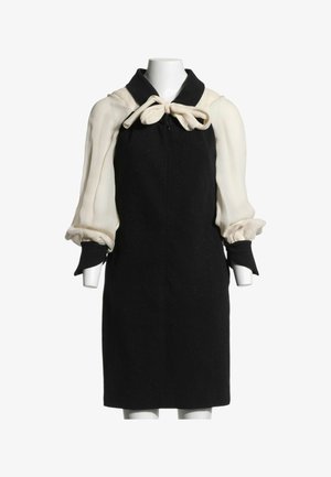 Robe noire sans manches avec de longues manches bouffantes couleur crème et un nœud crème noué au col sur un torse de mannequin blanc.
