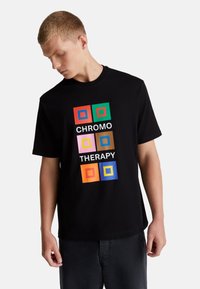 Camiseta negra de manga corta con un diseño gr�áfico que presenta cuadrados de colores y el texto "TERAPIA DEL COLOR" en fuente blanca.