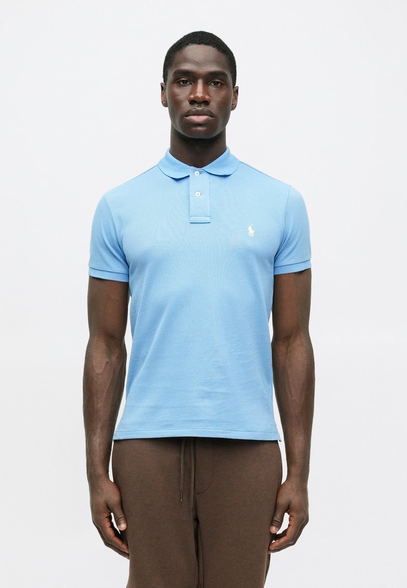 Lichtblauw poloshirt met een kraag, korte mouwen en een klein embleem op de linkerborst; de stof lijkt gestructureerd en ademend.